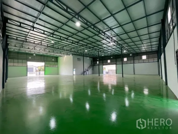 工厂 出租或出售在Bang Phli, Samut Prakan - 宽敞仓库内部，钢结构屋顶，明亮照明，卷闸门与高承重绿色地坪。