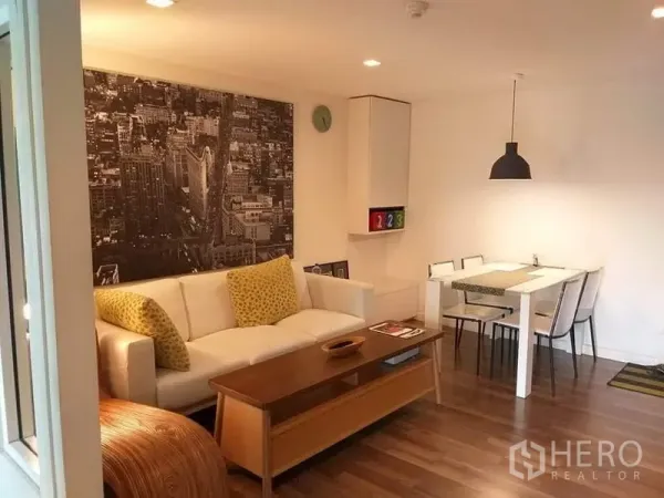 Condominium for rent in Watthana, Bangkok - Bright living and dining area with a white sofa, cityscape wall art, and warm wood flooring.