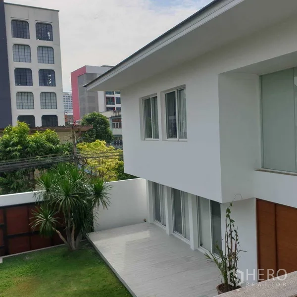 Detached House for rent in Watthana, Bangkok - Two-storey white detached house with wide terrace and lawn enclosed by a privacy wall, city buildings beyond.