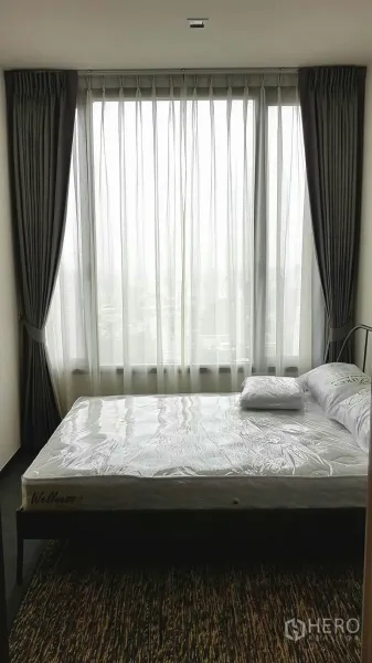 Condominium for rent in Watthana, Bangkok - Bedroom with large window, blackout drapes and a neatly made bed.