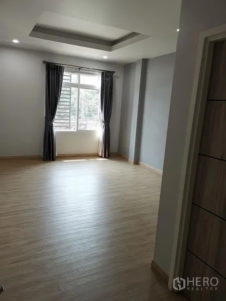 Detached House for rent in Chatuchak, Bangkok - Bright bedroom with wood-look flooring, tray ceiling, and a window with dark curtains.