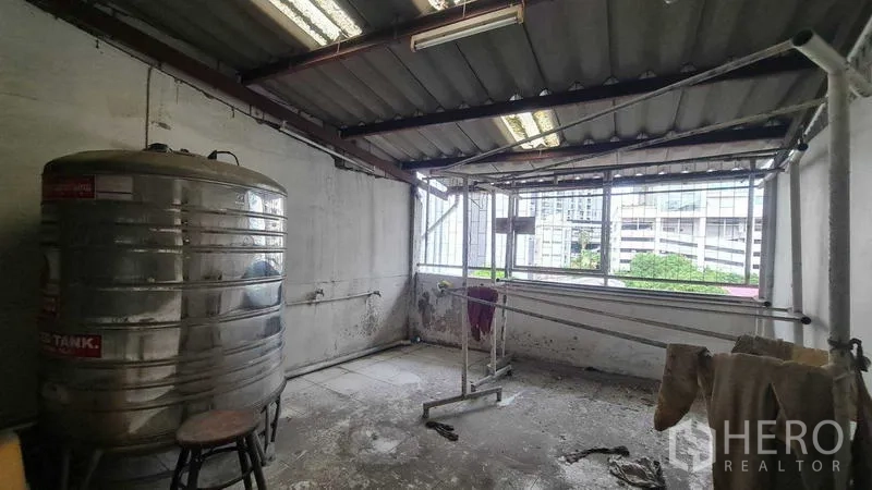 Shophouse for sale in Watthana, Bangkok - Rooftop utility area featuring a metal water tank, open windows, and laundry lines.