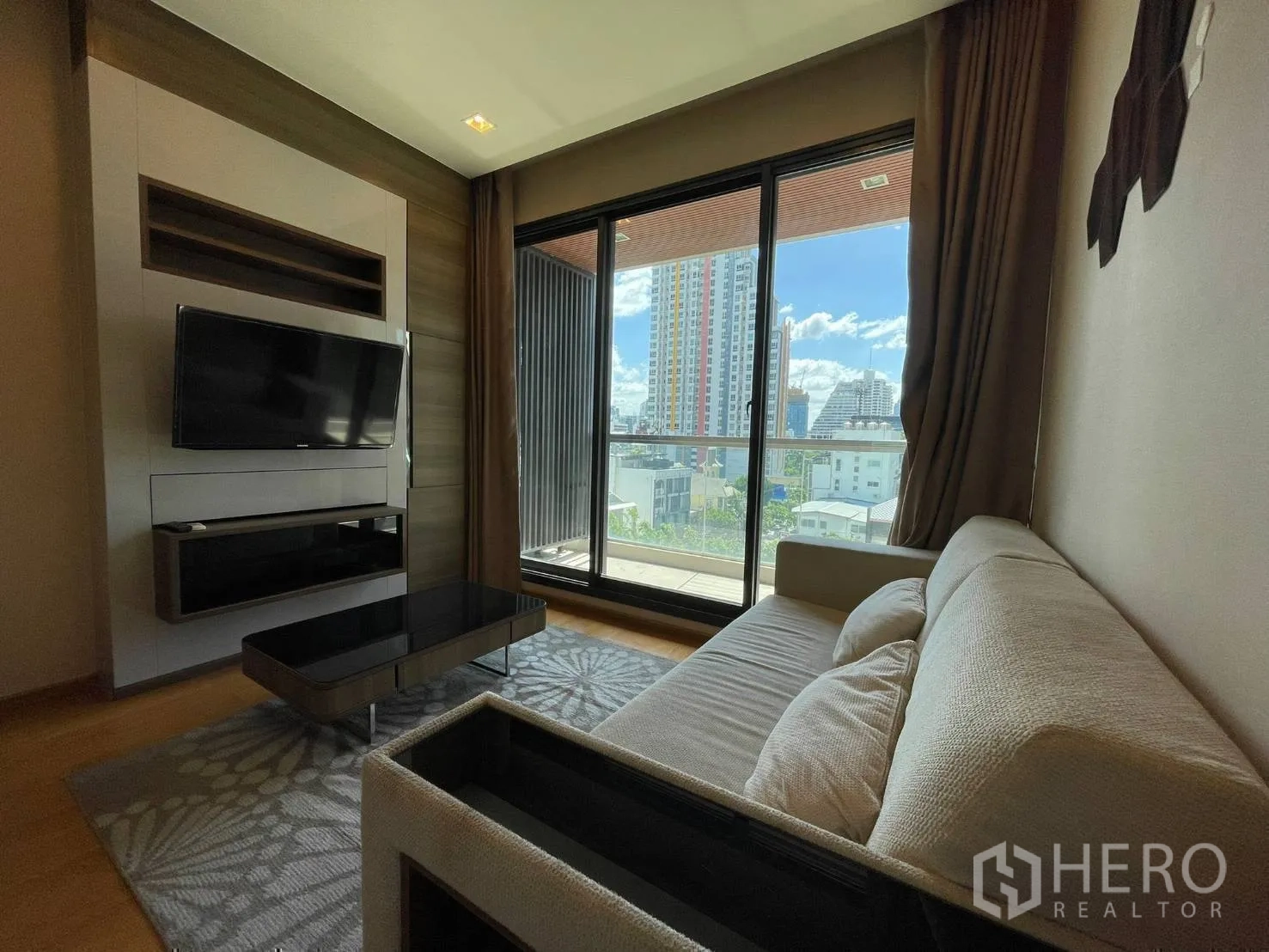Condominium for rent or sale in Bang Rak, Bangkok - Living room with sofa, wall-mounted TV and sliding glass doors to balcony.
