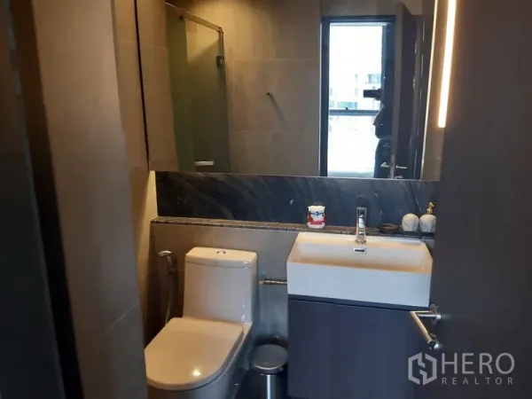 Condominium for rent or sale in Khlong Toei, Bangkok - Modern bathroom with glass shower, wide mirror and square vanity sink.