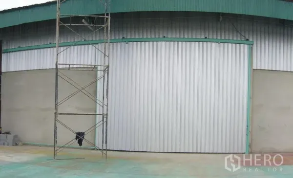 货栈 出租在Mueang Pathum Thani, Pathum Thani - 仓库外立面，宽大的金属推拉门与青绿色屋檐，前方为混凝土地面。