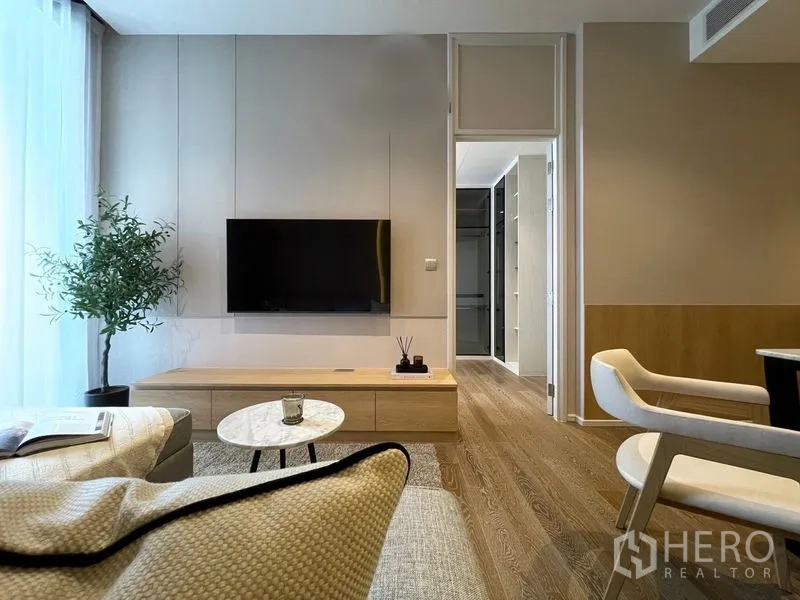 คอนโด ให้เช่าหรือขายในPathum Wan, Bangkok - มุมนั่งเล่นพร้อมทีวีติดผนัง ตู้ล่าง ทางเข้าห้องเก็บเสื้อผ้า พื้นไม้ และแสงจากระเบียง