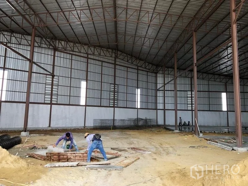 Warehouse for rent or sale in Sai Noi, Nonthaburi - High-clearance warehouse shell with steel columns and unfinished ground.