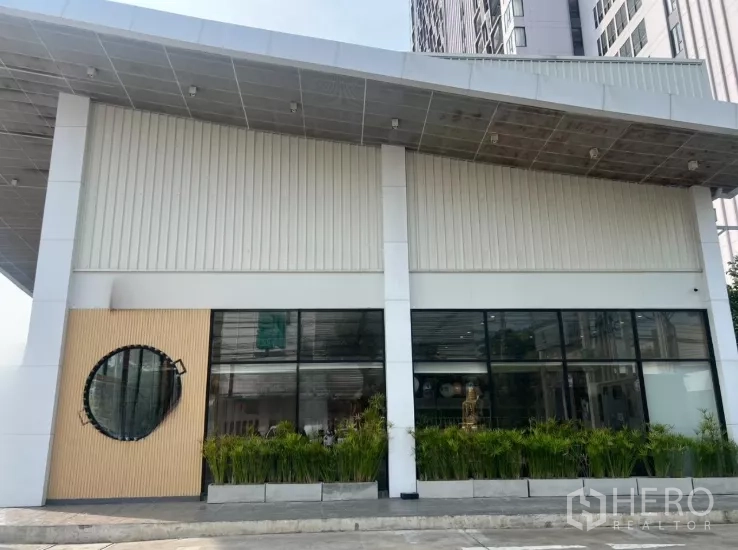 พื้นที่ขายปลีก ให้เช่าในWatthana, Bangkok - ด้านหน้าอาคารทันสมัย หลังคายื่น หน้าต่างวงกลม และแปลงต้นไม้จัดสวน.