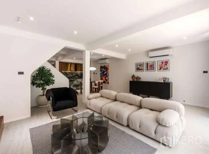 Townhouse for sale in Sathon, Bangkok - Living room with plush sofa, glass coffee table and recessed ceiling lights.