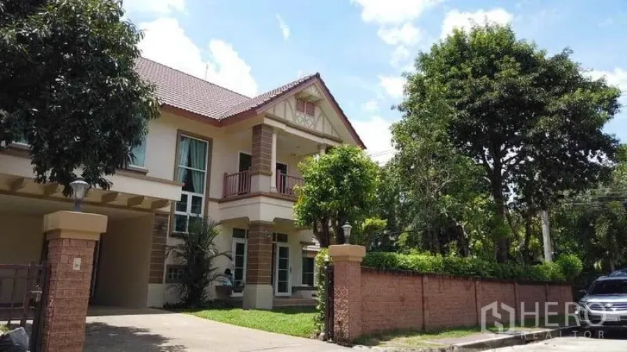 独立式住宅 出租或出售在Pak Kret, Nonthaburi - 街景视角的两层住宅，砖砌围墙、车道与绿树相映成趣。