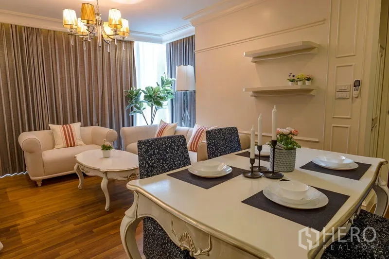 Condominium for rent in Watthana, Bangkok - View from dining to living area with warm lighting, wall shelves and large windows dressed with curtains.