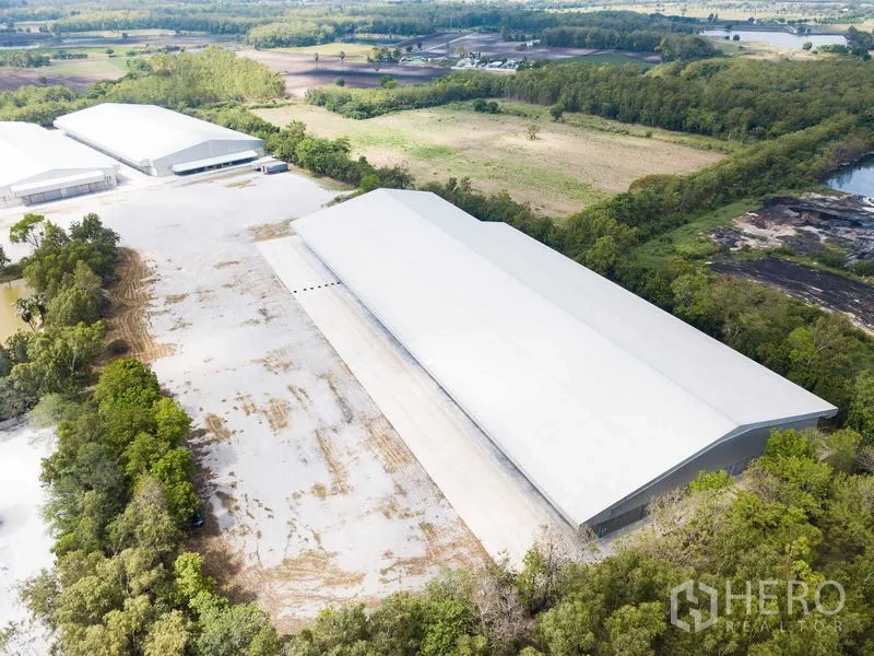 Warehouse for rent in Phra Phutthabat, Saraburi - Drone view of multiple large warehouses on a spacious plot bordered by trees and access roads.