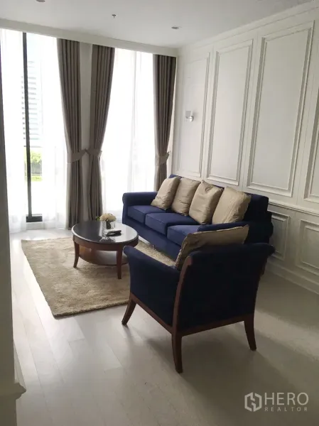 公寓 出租在Pathum Wan, Bangkok - 采光充足的客厅，海军蓝沙发、墙面线条与落地窗帘。