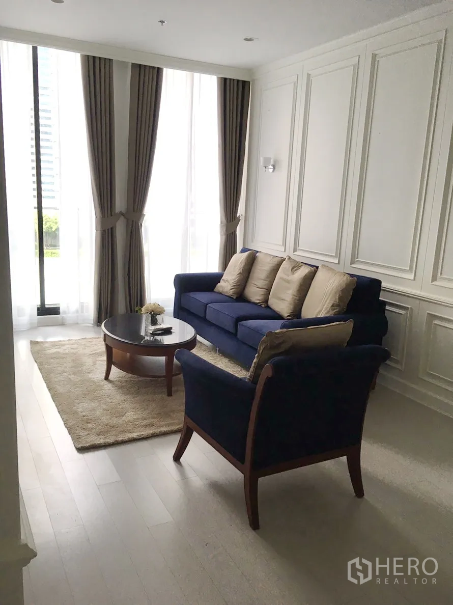 คอนโด ให้เช่าในPathum Wan, Bangkok - ห้องนั่งเล่นสว่างด้วยหน้าต่างสูง เฟอร์นิเจอร์โซฟาสีน้ำเงินและผนังบัวคลาสสิก