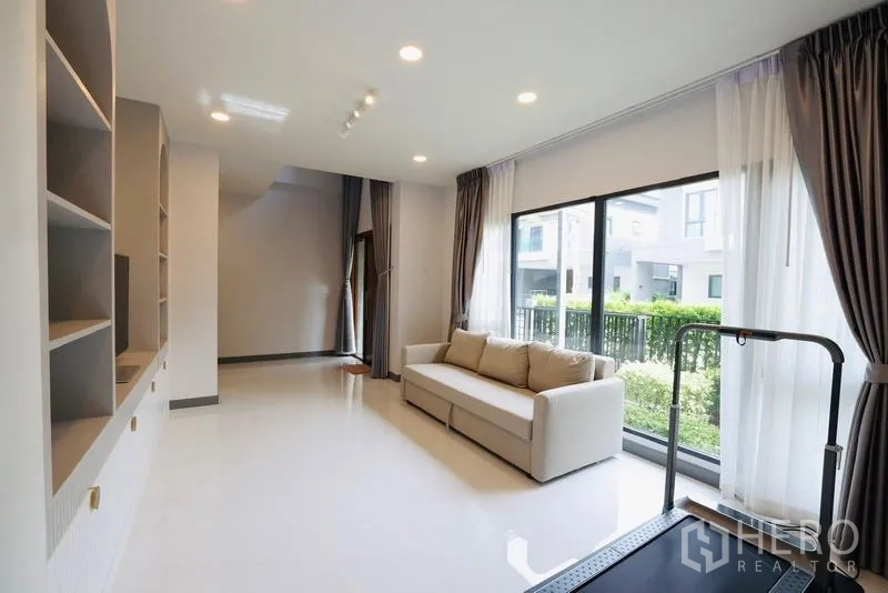 Detached House for rent in Bang Phli, Samut Prakan - Lounge room with sofa and treadmill beside floor-to-ceiling windows facing the garden.