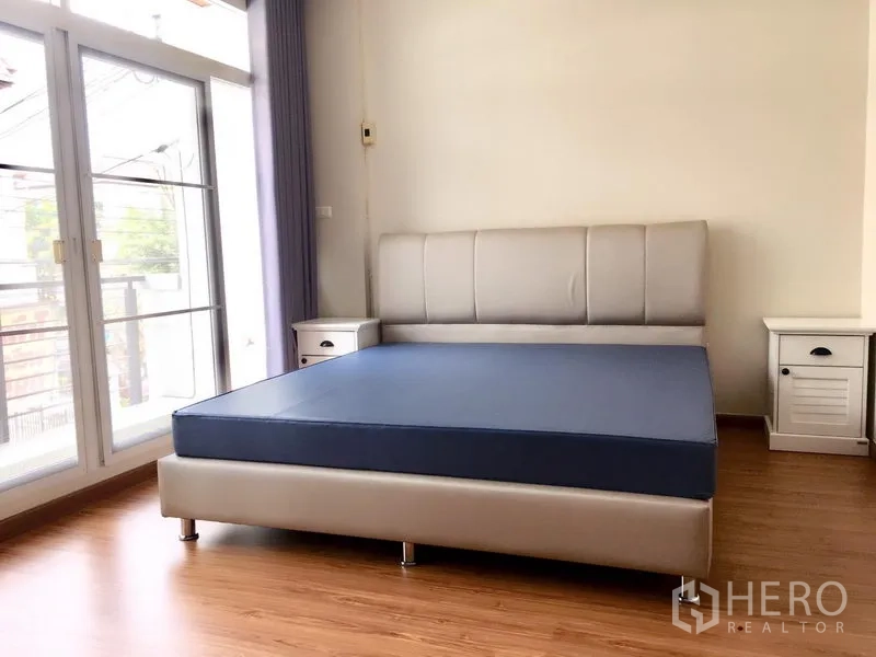 ทาวน์เฮาส์ ให้เช่าในPrawet, Bangkok - ห้องนอนใหญ่มีประตูบานกระจกเปิดสู่ระเบียงและโต๊ะข้างเตียง.