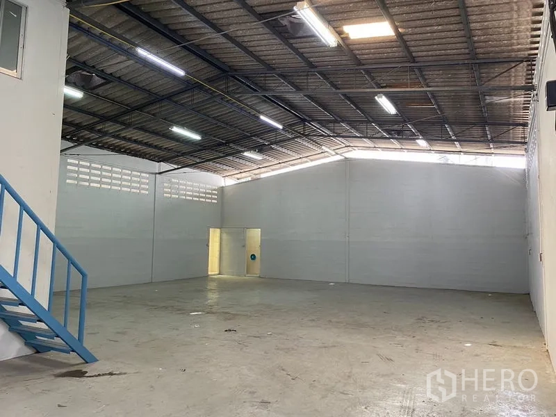 Warehouse for rent in Chatuchak, Bangkok - Clear‑span warehouse interior with high gable roof and fluorescent lighting.