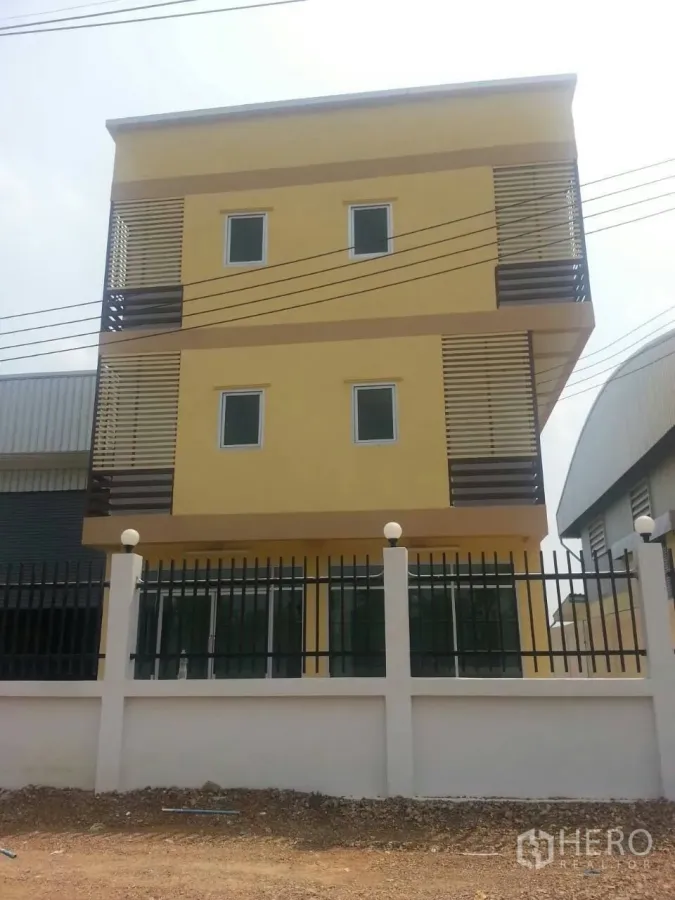 Factory for rent or sale in Khlong Luang, Pathum Thani - Three‑storey yellow factory office building with slatted balconies and a secure metal fence.