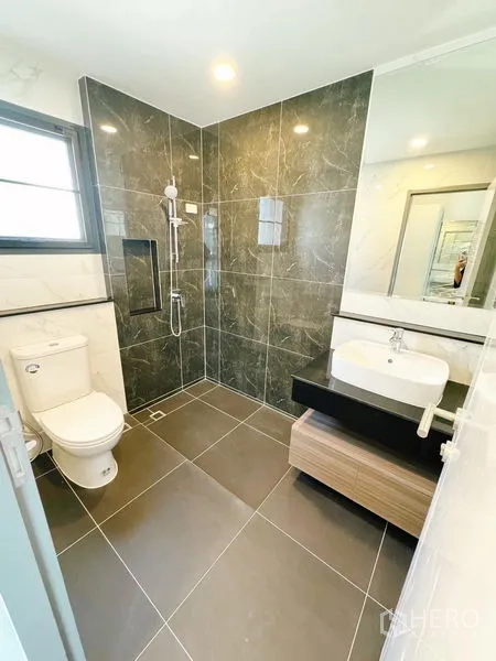 Detached House for rent in Bang Phli, Samut Prakan - Modern bathroom with dark tiled shower, toilet and vanity beneath a wide mirror.