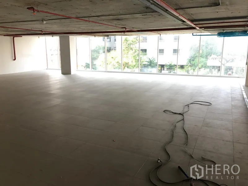 พื้นที่ขายปลีก ให้เช่าในKhlong Toei, Bangkok - โถงร้านค้ากว้าง เพดานดิบ พร้อมกระจกเต็มผนังรับแสงธรรมชาติและวิวต้นไม้ด้านนอก.