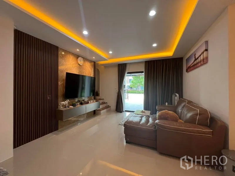 ทาวน์เฮาส์ ให้เช่า - ห้องนั่งเล่นโทนอบอุ่น โซฟาหนัง ผนังทีวีตกแต่ง และไฟซ่อน พร้อมประตูกระจกบานเลื่อน