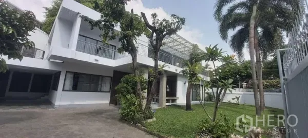 Detached House for rent in Pathum Wan, Bangkok - Two-storey white detached house with lawn, trees, and a gated driveway.