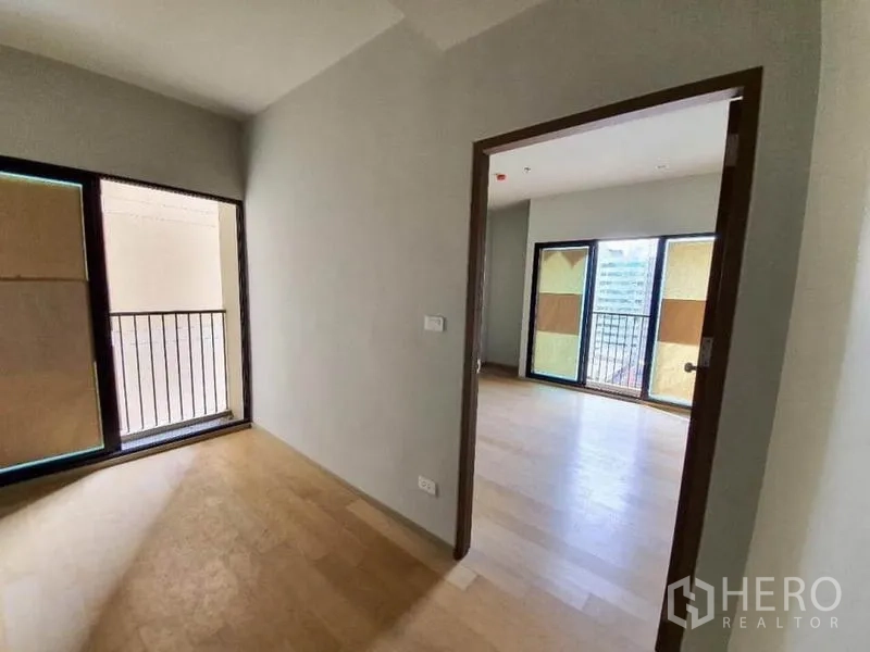 Condominium for sale in Ratchathewi, Bangkok - Compact room with door to balcony connecting to a brighter living space with large windows.