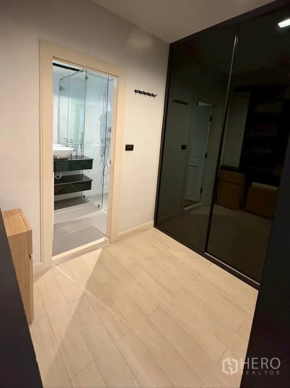 联排别墅 for rent in Pathum Wan, Bangkok - 浅木地板房间，深色玻璃衣柜，通往浴室的门。