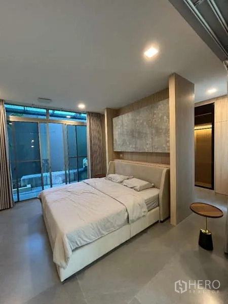 Detached House for rent in Saphan Sung, Bangkok - Spacious bedroom with neutral headboard, side table and sliding doors to terrace.