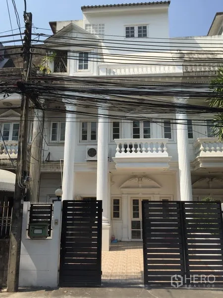 ทาวน์เฮาส์ ให้เช่าในChatuchak, Bangkok - ด้านหน้าทาวน์เฮ้าส์สีขาวหลายชั้น เสากรีก ระเบียง และประตูรั้วสีดำ ย่านจตุจักร