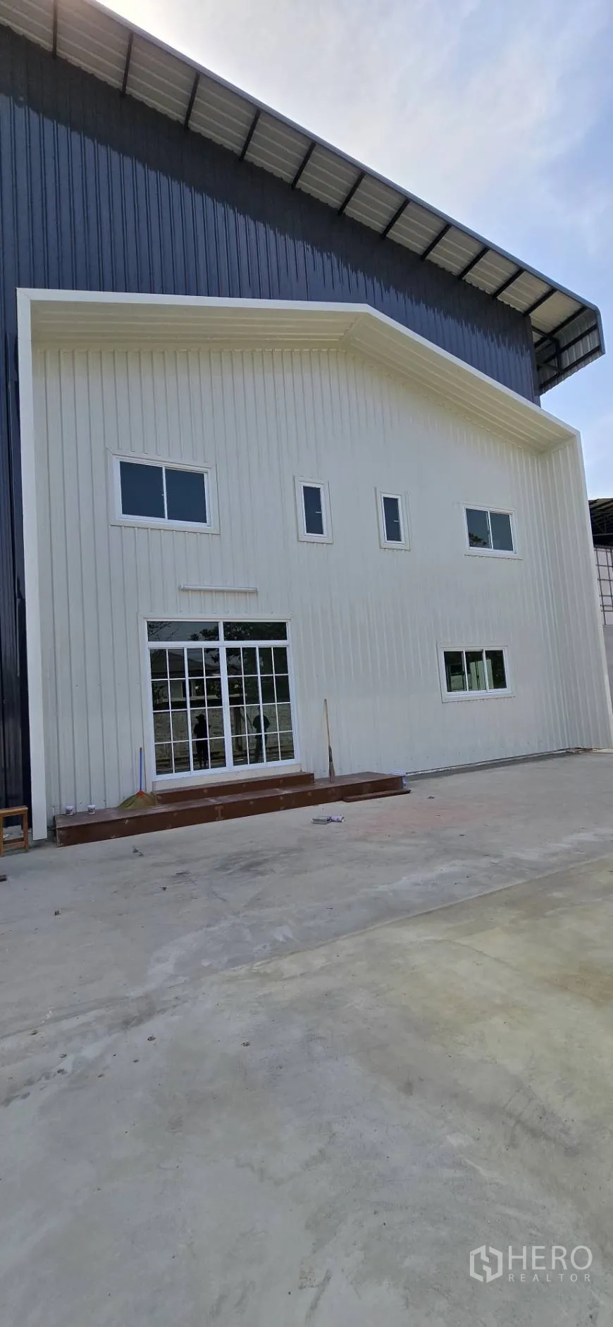 Factory for rent in Mueang Samut Sakhon, Samut Sakhon - Front facade of the attached white office section with large glass doors and windows opening to a paved yard.