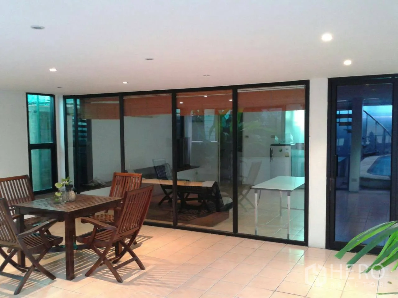 Detached House for rent in Suan Luang, Bangkok - Covered terrace with wooden dining set and sliding glass doors facing the pool.