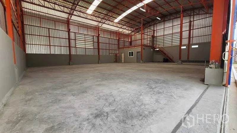 Warehouse for rent in Nong Chok, Bangkok - Warehouse interior from the entrance showing office box, staircase, and skylight panels.