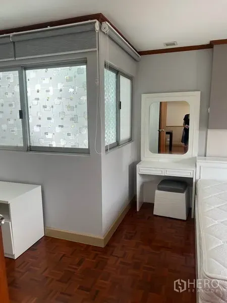 Condominium for rent in Watthana, Bangkok - Corner bedroom area with dressing table, stool and windows fitted with privacy blinds.