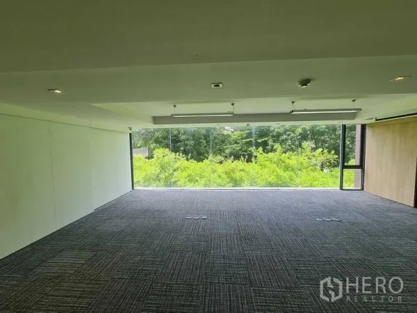 Office Space for rent in Watthana, Bangkok - Spacious office floor with panoramic glass overlooking trees, dark carpet tiles, floor outlet boxes and ceiling LED fixtures.