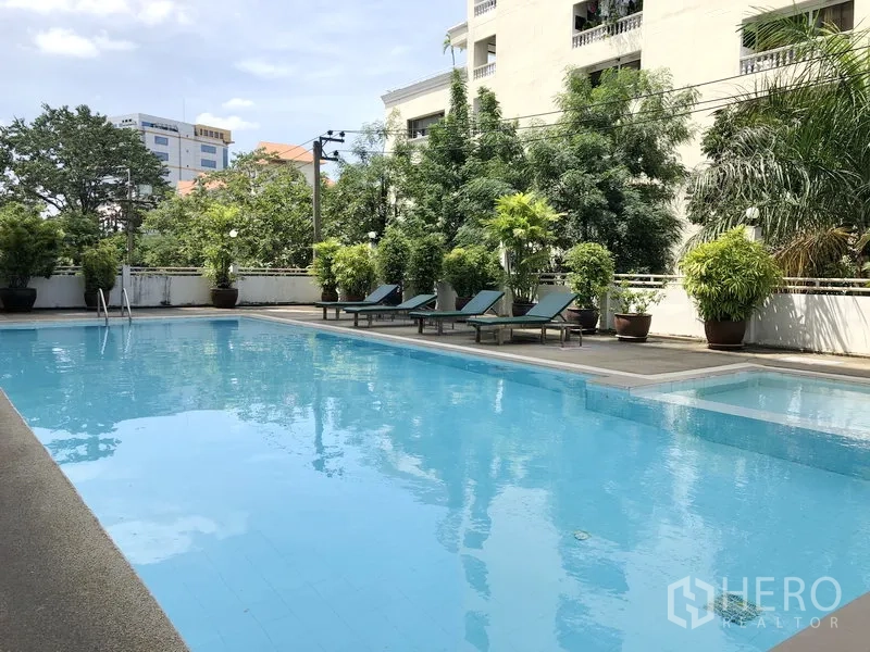 Apartment for rent in Suan Luang, Bangkok - Outdoor swimming pool with sun loungers, lush greenery and a low-rise building backdrop.