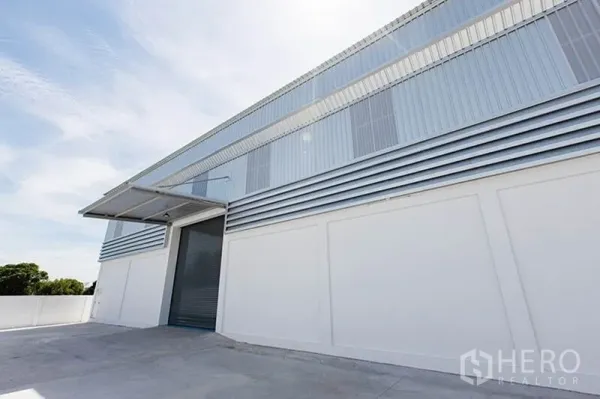 โรงงาน ให้เช่าในBang Phli, Samut Prakan - มุมมองด้านข้างของโกดังด้วยผนังเมทัลชีท หลังคาสูง และทางโหลดสินค้าพร้อมประตูม้วน