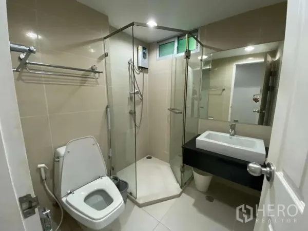 Condominium for  in Huai Khwang, Bangkok - Modern bathroom with glass shower enclosure, vanity sink and toilet finished in beige tiles.