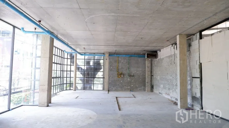 零售空间 出租在Watthana, Bangkok - 宽敞毛坯室内，混凝土顶与管线可见，转角玻璃适合显眼招牌。