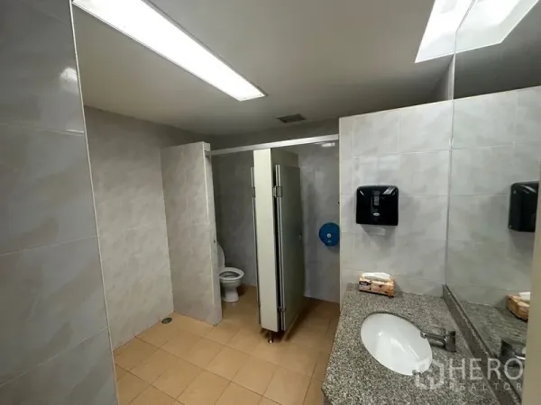 Office Space for rent in Khlong Toei, Bangkok - Shared office restroom with stalls, sink, mirror and tiled walls under fluorescent lighting.