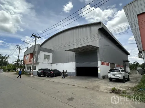 工厂 出租在Phra Nakhon Si Ayutthaya - 街景视角的大型钢板外墙工厂，弧形屋顶，宽阔卷闸门与前方停车位。