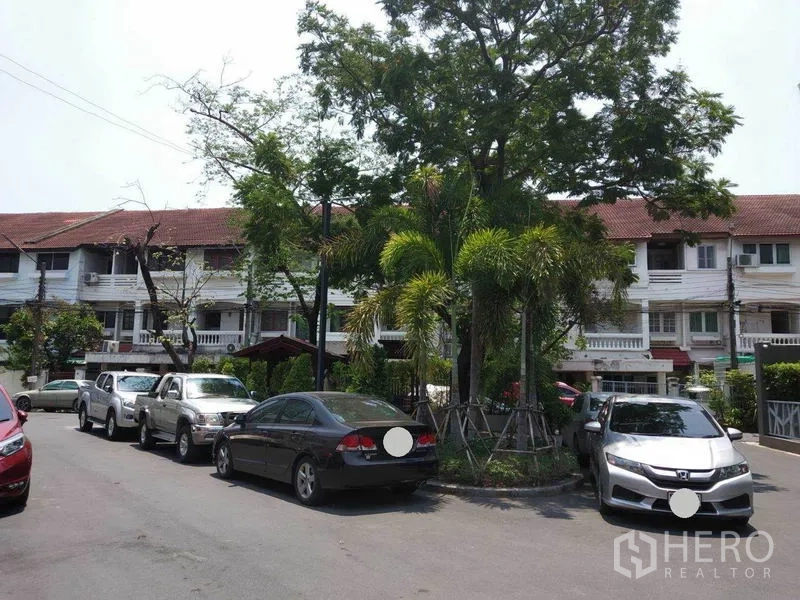 联排别墅 出租或出售在Wang Thonglang, Bangkok - 社区街景，中央绿化岛、棕榈树、路边停车与联排住宅。
