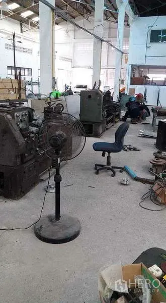 Warehouse for rent or sale in Nong Suea, Pathum Thani - Open production floor with machinery, a fan and chair under a high roof.
