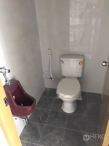 零售空间 出租在Bang Kapi, Bangkok - 卫生间配坐便器、小便池与喷枪，灰色地砖铺设。