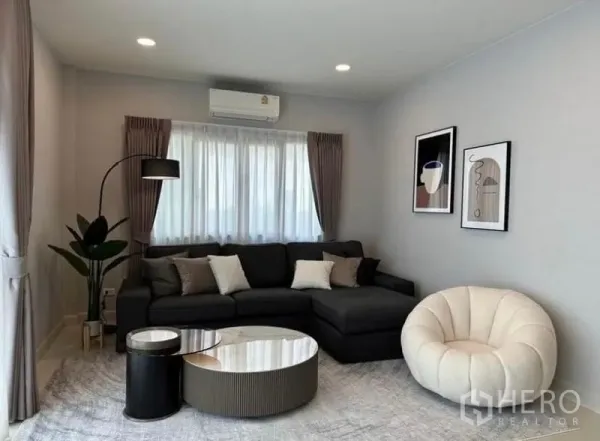 Detached House for rent in Bang Phli, Samut Prakan - Bright living room with L-shaped sofa, round accent chair, floor lamp and curtained windows.