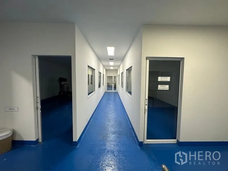 Warehouse for rent in Pak Kret, Nonthaburi - Long, bright hallway with windows into clean rooms and labeled doors for production workflow.