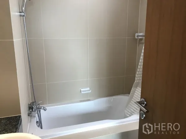 Condominium for rent in Watthana, Bangkok - Bathroom with beige tiles, bathtub, and handheld shower.