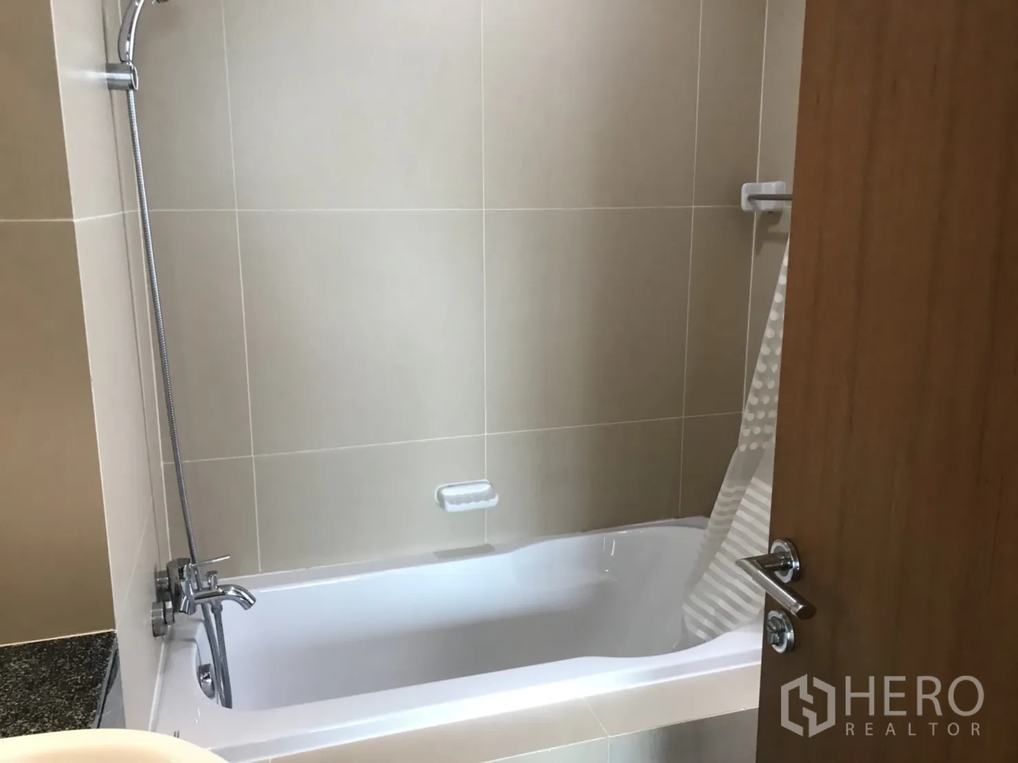 Condominium for rent in Watthana, Bangkok - Bathroom with beige tiles, bathtub, and handheld shower.
