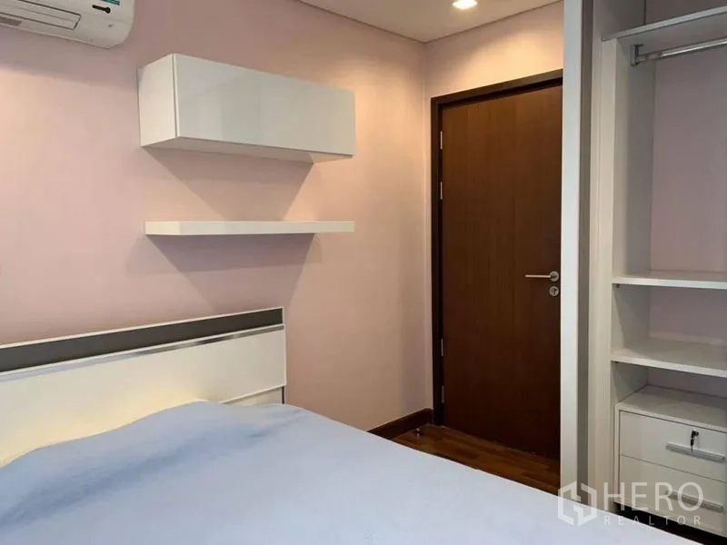 Condominium for rent in Watthana, Bangkok - Second bedroom with shelves, wardrobe and soft pastel walls.