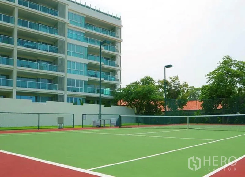 Condominium for sale in Bang Lamung, Chon Buri - Modern mid-rise condominium with glass balconies beside an outdoor tennis court.